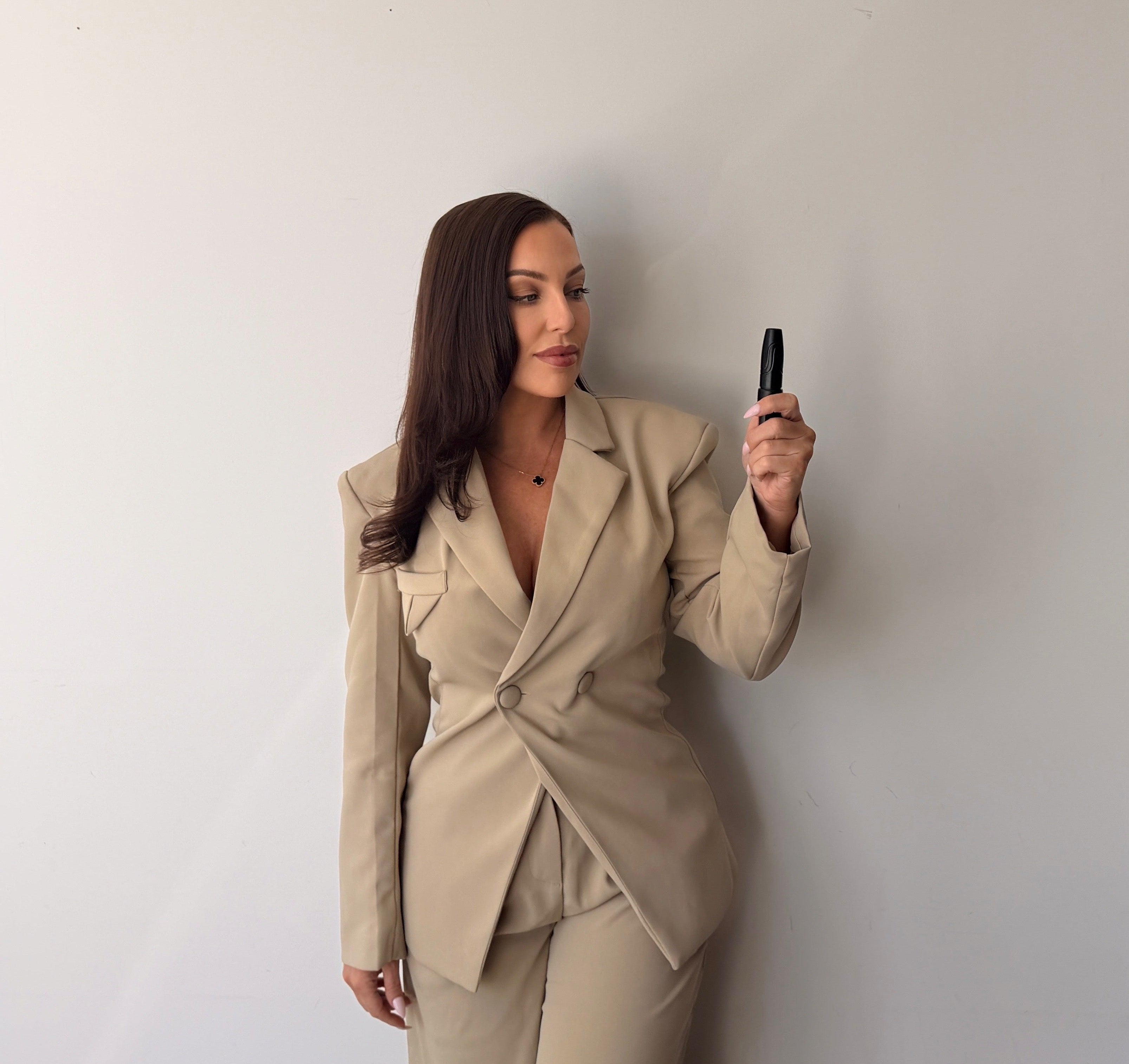 Woman in a beige suit standing against a white wall, holding a PMU machine.